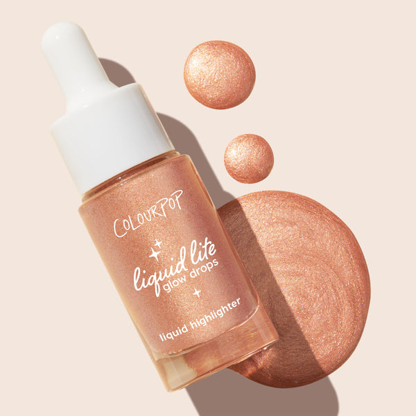 ColourPop Liquid Highlighter Venice Blvd bottle with white dropper rests diagonally, spilling pearly rose-gold glow drops and a swirled swatch on a light beige background, showcasing Liquid Lite Glow Drops' radiant, buildable finish.