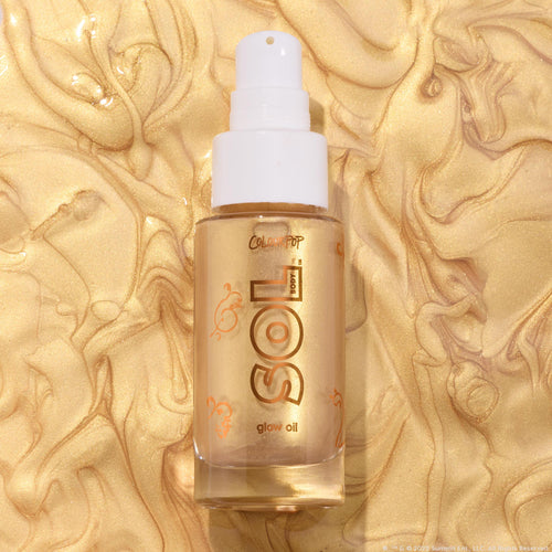 Clear glass bottle of ColourPop SOL Glow Oil, It’s a Wolf Thing, standing upright with a white pump and gold SOL logo, showcasing shimmering golden body oil against a swirled metallic gold backdrop.