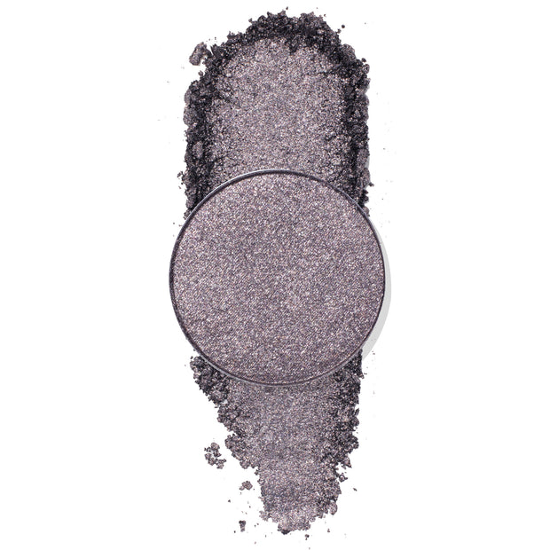 Goody Two-Shoes pressed powder shadow by ColourPop - shimmery gunmetal-lilac eyeshadow pan - rests over a vertical swipe of crushed pigment, showcasing its metallic sparkle on a clean white background.