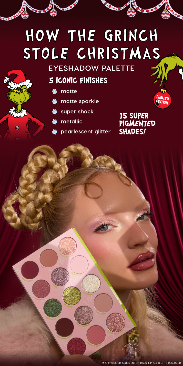 ColourPop How the Grinch Stole Christmas eyeshadow palette held by a model against a burgundy holiday backdrop, showing pink palette with lime trim and 15 shades: matte, matte sparkle, metallic, Super Shock, and pearlescent glitter, limited edition.