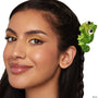 ColourPop Tangled Pascal Hair Clip holding a side braid, the glossy green chameleon hair accessory with a coiled tail clipped above the ear, shown on a model with shimmering gold eyeshadow and nude gloss against a white background.