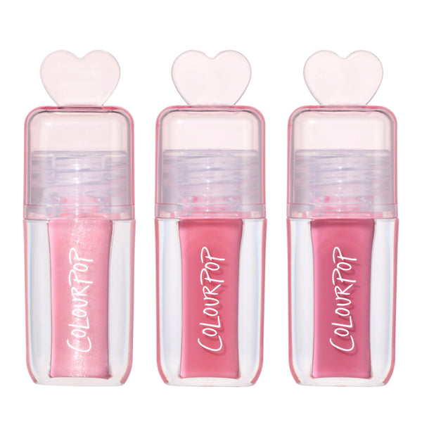 Three ColourPop Gloss Me Up ultra glossy lip set tubes from the Heart to Get collection standing upright, each in a clear pink case with heart-shaped cap and varying pink gloss shades on a clean white background.