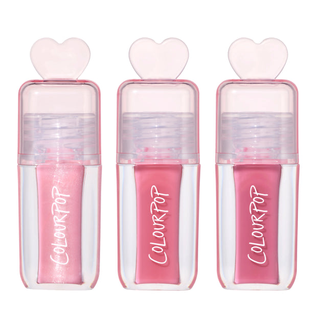 Three ColourPop Gloss Me Up ultra glossy lip set tubes from the Heart to Get collection standing upright, each in a clear pink case with heart-shaped cap and varying pink gloss shades on a clean white background.