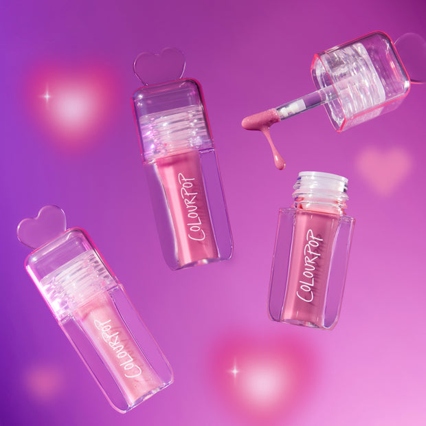 Gloss Me Up ultra glossy lip set from the Heart to Get collection, with three pink ColourPop lip gloss tubes and a dripping applicator floating on a glowing pink and purple background with heart-shaped caps.
