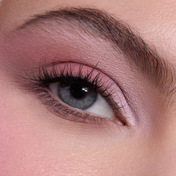 Close-up of a blue-gray eye wearing soft pink shimmer and matte shadows from the Heart to Get shadow palette, with long defined lashes and groomed brow showcasing a romantic everyday eye look for US makeup lovers.