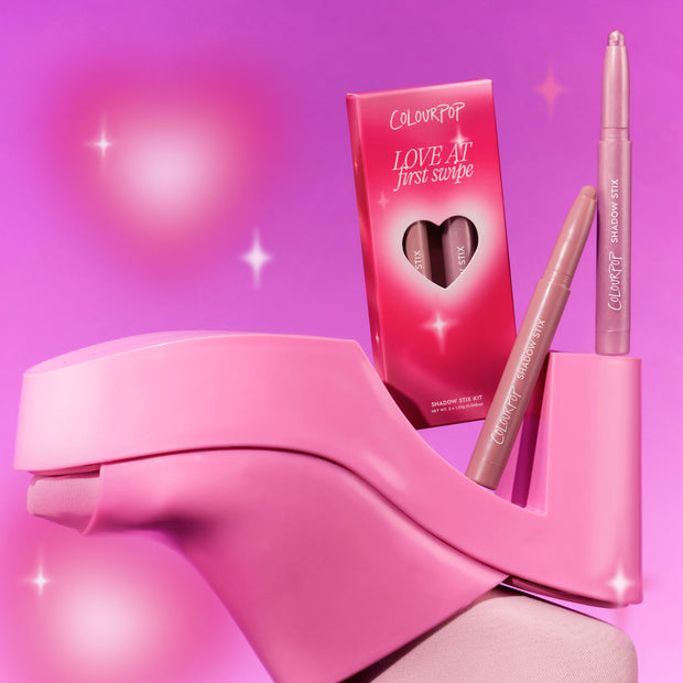 ColourPop Love At First Swipe Shadow Stix from the Heart to Get collection standing upright beside its heart-cutout pink box, styled on a chunky pink high heel against a glowing pink background for a playful makeup product shot.