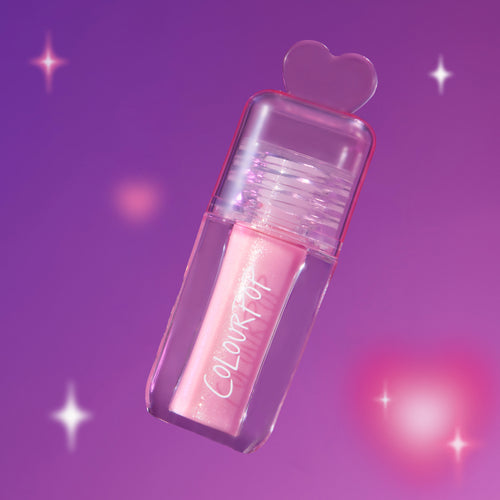 ColourPop 2 Die 4 Ultra Glossy Lip in a clear tube with pink shimmer gloss and heart-shaped cap floating against a dreamy purple Heart to Get themed background with soft sparkles.