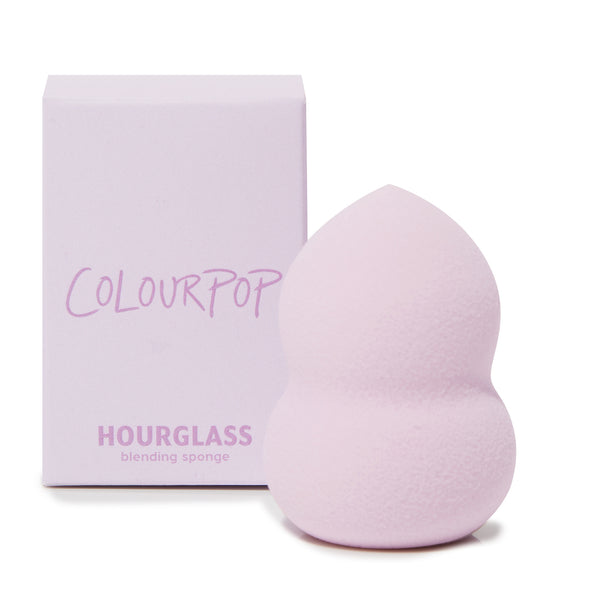 Hourglass Blending Sponge blending foundation and concealer with a pointed tip and curved hourglass grip, shown upright beside a lavender ColourPop box; soft pastel purple foam, a ColourPop Makeup Tools & Accessories staple for seamless coverage.