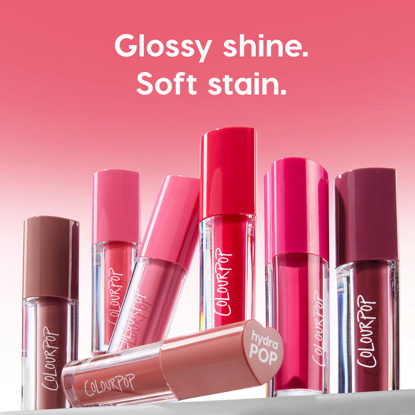 Colourpop Blueberry Marg lip stain from the Hydra Pop collection standing among other glossy lipstick & lip stains in pink and berry tubes, under bold text reading “Glossy shine. Soft stain.” against a pink gradient background.