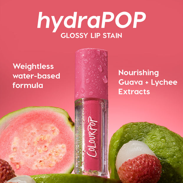 Baby Fox ColourPop Lip Stain hydraPOP glossy tube, beaded with dew, stands among fresh guava and lychee on a pink backdrop, highlighting guava + lychee extracts and a weightless water-based, hydration-infused color in vibrant pink.