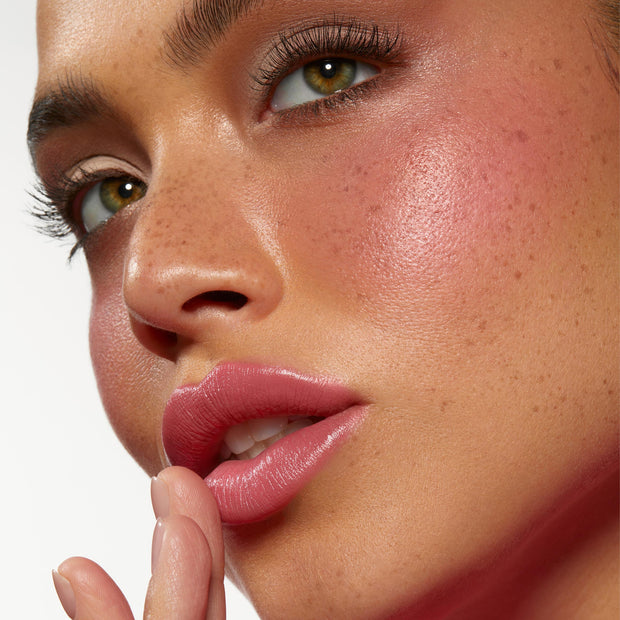 Model’s lips and cheeks wearing Adore You ColourPop Lip and Cheek Balm, delivering a buildable rosy‑pink flush and glossy hydration in a close-up beauty shot against a clean white background.