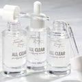 Fourth Ray Beauty All Clear Purifying Serum, a ColourPop Face Serum, three clear 0.85 fl oz (25 mL) glass dropper bottles with pipettes releasing transparent drops on a bright white surface.