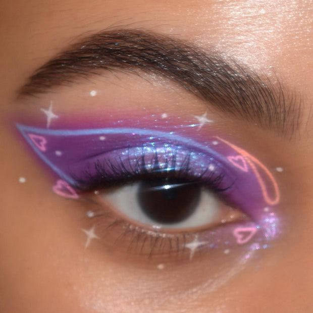 ColourPop BFF Liquid Liner in Graceland drawing a crisp white graphic wing across a close-up eye, layered over iridescent purple shimmer shadow with sparkles and heart doodles, highlighting precise payoff and clean edges.