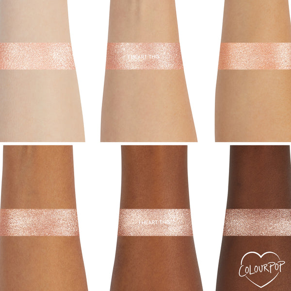 ColourPop I Heart This Super Shock Shadow swatch shows a wide shimmery champagne band across six arms from light to deep skin tones, highlighting even payoff and sparkle, with a small ColourPop heart logo in the corner.