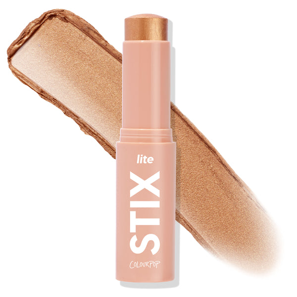 ColourPop Lite Stix in Ignite stands uncapped with the cream highlighter bullet exposed, shown beside a broad swipe of its warm golden shimmer; peach tube labeled “lite STIX” on a clean white background.