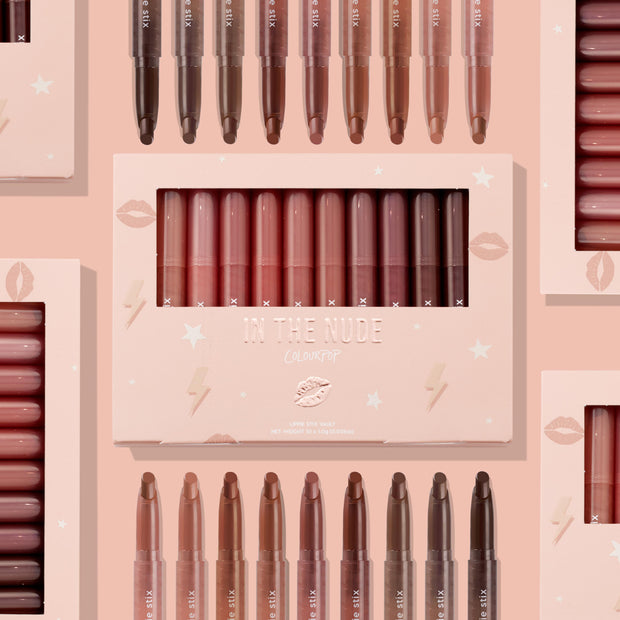 ColourPop Lippie Stix In the Nude vault displaying 10 nude shades - peach to deep cocoa - lined upright in a blush pink window box with star and lip icons, with additional Lippie Stix arranged around it on a soft pink backdrop.