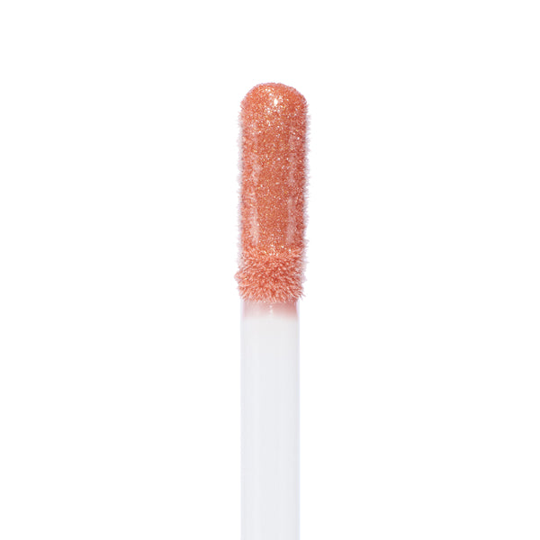 Doe-foot applicator coated in It Girl Ultra Glossy Lip, a peachy-pink shimmer with fine gold flecks, catching light in a macro close-up - ColourPop Ultra Glossy Lip on a clean white background showing its high-shine, creamy texture.