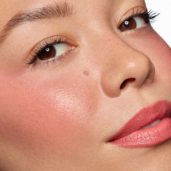 Rosy cheeks and tinted lips wearing ColourPop Lip and Cheek Balm in It’s a Look, showing a dewy, hydrated sheen and soft pink flush; extreme close-up face in studio light highlights smooth texture and natural, buildable color.
