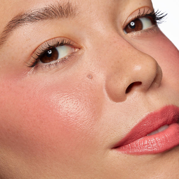 Rosy cheeks and tinted lips wearing ColourPop Lip and Cheek Balm in It’s a Look, showing a dewy, hydrated sheen and soft pink flush; extreme close-up face in studio light highlights smooth texture and natural, buildable color.