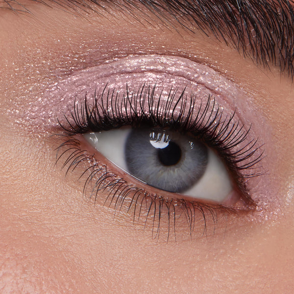 Macro close-up blue eye showcasing Boo-Kay ColourPop Jelly Much Shadow, a shimmery mauve-pink gel eyeshadow swept across the lid and crease with a wet metallic finish, accenting natural lashes and a groomed brow in studio lighting.