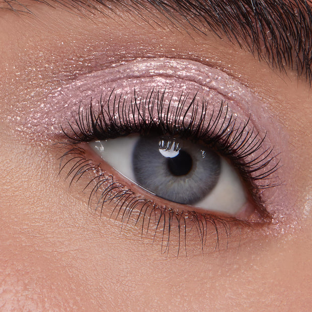 Macro close-up blue eye showcasing Boo-Kay ColourPop Jelly Much Shadow, a shimmery mauve-pink gel eyeshadow swept across the lid and crease with a wet metallic finish, accenting natural lashes and a groomed brow in studio lighting.