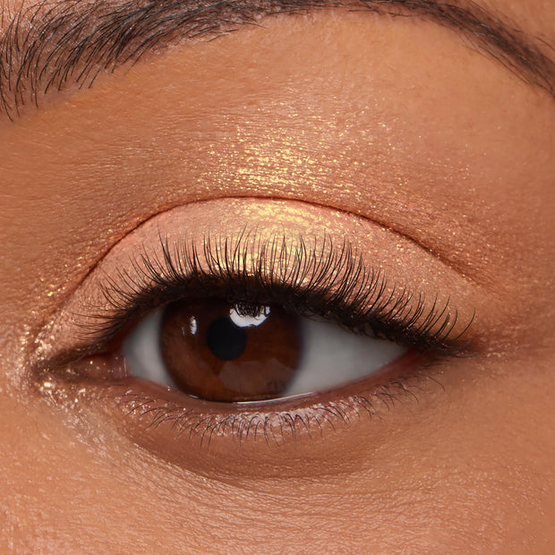 ColourPop Jelly Much Shadow in Buzzy shimmering across a brown eyelid, reflecting peachy-gold metallic glow, shown in a macro close-up with natural lashes under studio lighting.