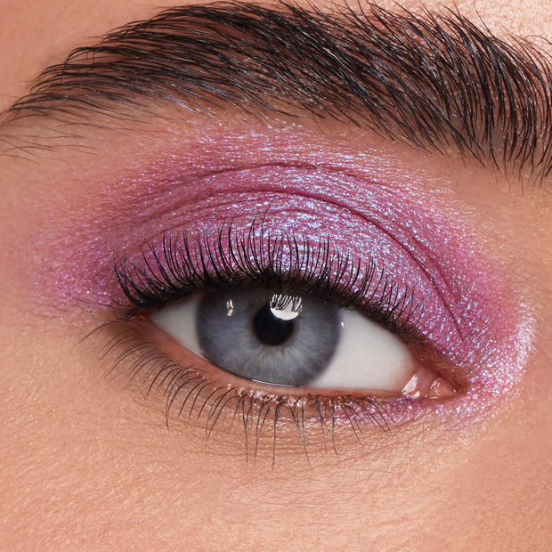 Blue eye wears ColourPop Jelly Much Shadow in Duckling, a jelly metallic lilac-pink eyeshadow shimmering across the lid, showing smooth, high-shine payoff in a macro close-up with defined lashes and a groomed brow.