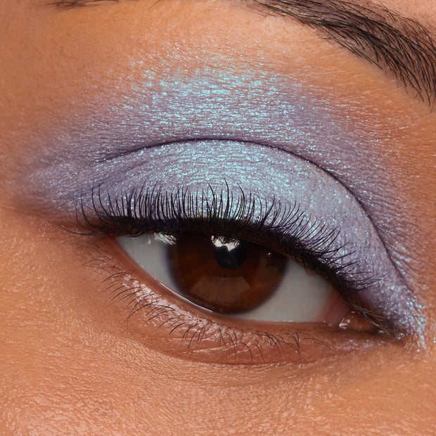 Iridescent blue‑lavender eyeshadow sweeping a brown eye’s lid, showcasing Hallucinogenius Jelly Much Shadow’s metallic duochrome sheen; macro close-up highlighting the smooth, opaque payoff and sparkle of ColourPop Jelly Much Shadow.