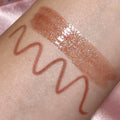 Best Besties ColourPop Ultra Lip Duo swatched on inner arm - shimmering nude gloss with gold micro-shimmer beside a warm rosy-brown liner squiggle - showing texture, shine, and payoff against a soft pink satin background.