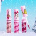 Colourpop x The Grinch Merry Grinchmas Swirl Lip Gloss Kit - three swirl gloss tubes with pink caps featuring Max, Cindy-Lou Who, and the Grinch - one wand open showing a rosy applicator, standing in snow with a blue sky and falling flakes.
