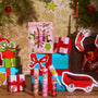 ColourPop Merry Grinchmas Swirl Lip Gloss Kit featuring a 3-piece set of pink-toned swirl lip glosses, one wand open, displayed in Grinch-themed packaging amid wrapped gifts and a lit fireplace for a festive holiday scene.