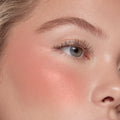 THX ColourPop Liquid Blush delivering a dewy peach sheen on the cheekbone, blending seamlessly on skin; close-up of a model’s eye and cheek showing soft glow and natural lashes under studio lighting.