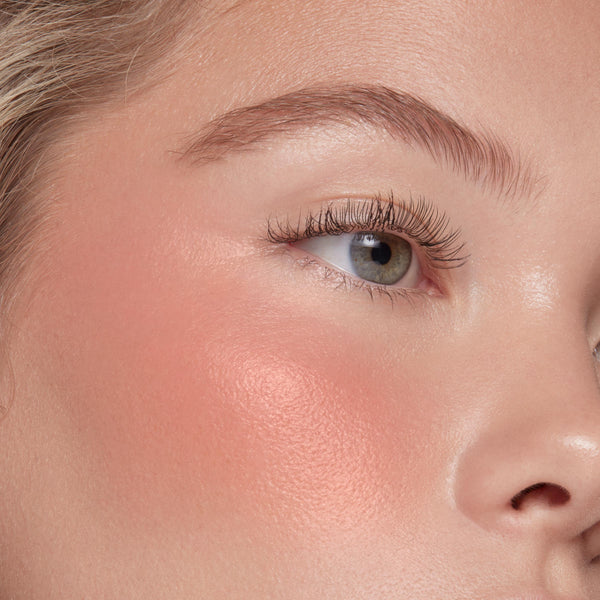 THX ColourPop Liquid Blush delivering a dewy peach sheen on the cheekbone, blending seamlessly on skin; close-up of a model’s eye and cheek showing soft glow and natural lashes under studio lighting.
