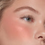 THX ColourPop Liquid Blush delivering a dewy peach sheen on the cheekbone, blending seamlessly on skin; close-up of a model’s eye and cheek showing soft glow and natural lashes under studio lighting.