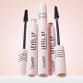 ColourPop Lengthening Mascara Level Up in Black stands upright with two uncapped wands revealing dense bristles, pale pink tubes marked with black stripes and logo on a soft pink backdrop, showcasing the sleek lash-lengthening product.