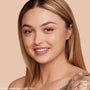 Model wearing Light 55 N neutral shade, showing smooth, dewy medium coverage from ColourPop Hyaluronic Hydrating Foundation in a close-up smile against a peach studio background.