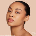 Model wearing Light 70 W, ColourPop Hyaluronic Hydrating Foundation, showing a smooth, dewy, warm‑toned complexion in a close-up studio portrait against a soft beige background.