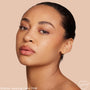 Model wearing Light 70 W, ColourPop Hyaluronic Hydrating Foundation, showing a smooth, dewy, warm‑toned complexion in a close-up studio portrait against a soft beige background.
