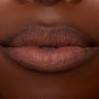 Lips wearing ColourPop Lippie Stix In the Nude, delivering creamy brown‑nude color with smooth, even coverage; macro studio close-up highlights hydrated texture and crisp lip line for an everyday lipstick look.