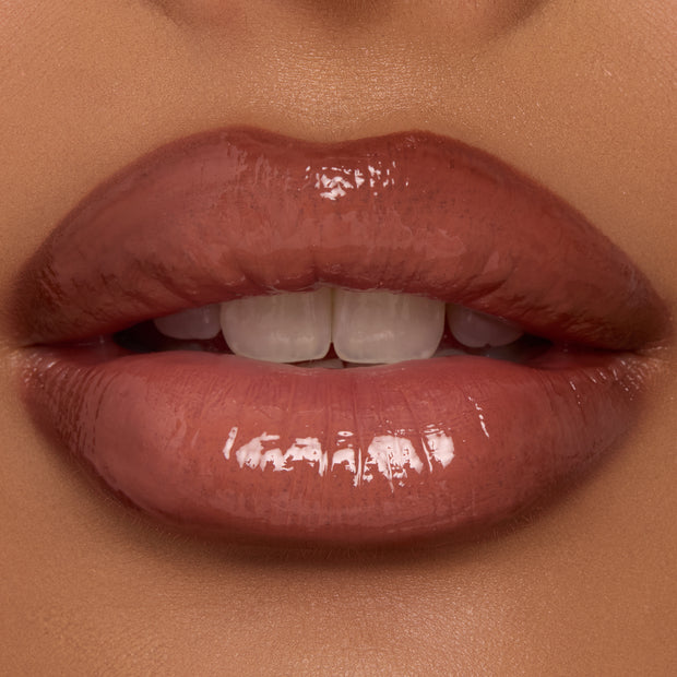 Lips wearing ColourPop Coffee Break Ultra Glossy Lip, a warm coffee-brown nude, reflecting high-shine gloss as they part slightly to reveal teeth in a tight close-up, showcasing smooth texture and even, full coverage.