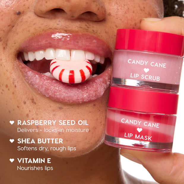 ColourPop Candy Cane Lip Scrub and Lip Mask jars stacked and held beside glossy lips coated with sugary scrub as a peppermint candy rests between teeth, showcasing a holiday lip care duo with raspberry seed oil, shea butter, and vitamin E benefits.