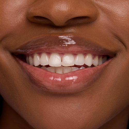 Glossy lips smile, wearing the Chocolate Milkshake ColourPop Lip Mask, delivering a clear, high-shine finish that smooths and hydrates; tight crop of mouth and teeth highlights the plush sheen for product detail.