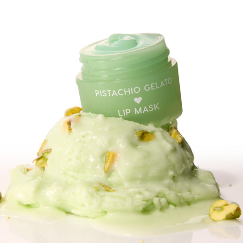 Mint-green Pistachio Gelato lip mask jar, lid off to reveal glossy balm, perched on a melting scoop of pistachio gelato with nut pieces on a white background - ColourPop Lip Mask product shot emphasizing creamy texture and dessert-inspired scent.