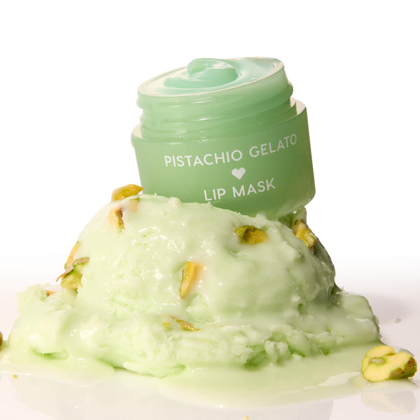 Mint-green Pistachio Gelato lip mask jar, lid off to reveal glossy balm, perched on a melting scoop of pistachio gelato with nut pieces on a white background - ColourPop Lip Mask product shot emphasizing creamy texture and dessert-inspired scent.
