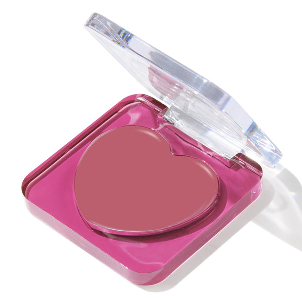 Heart-shaped rosy mauve balm set in a fuchsia acrylic compact with a clear flip lid, shown at a three-quarter angle on a white background; ColourPop Lip and Cheek Balm in the Love Interest shade, a multitasking tint for lips and cheeks.