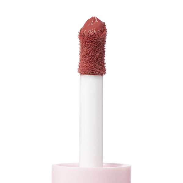 Doe-foot applicator coated in the creamy rosy-nude Culver City shade of ColourPop Liquid Blush, shown in macro close-up with a plush flocked tip rising from a soft pink tube against a clean white background.