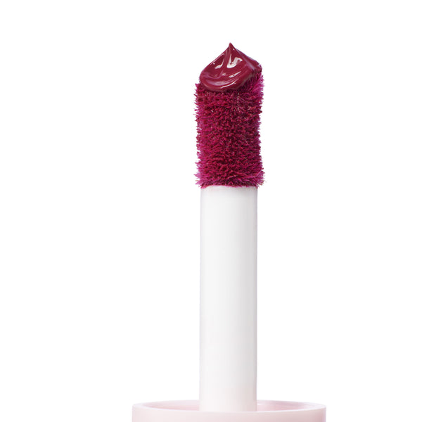 Doe-foot applicator deposits a glossy, deep berry dollop of Royal Flush ColourPop Liquid Blush, shown in close-up on a white background, highlighting the plush wand and precise tip for smooth, buildable cheek color.
