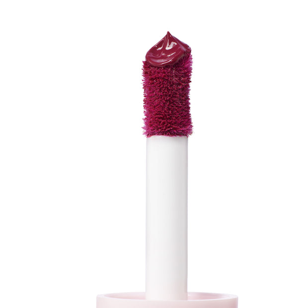 Doe-foot applicator deposits a glossy, deep berry dollop of Royal Flush ColourPop Liquid Blush, shown in close-up on a white background, highlighting the plush wand and precise tip for smooth, buildable cheek color.