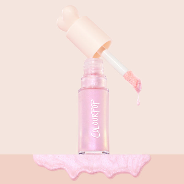 Pink Pony ColourPop Liquid Highlighter drips from a doe-foot applicator, the open clear bottle with cream heart-shaped cap set on a blush background above a glossy iridescent pink swatch.