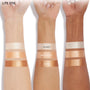Molten Hot Lite Stix swatched on three raised forearms, a warm metallic gold-peach cream highlighter between Glazey and Ignite, showing luminous payoff across light, medium, and deep skin tones on a white studio background; ColourPop Lite Stix.